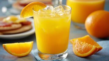 A vibrant glass of orange drink filled with ice sits on a table. Fresh orange slices are arranged beside it, accompanied by snacks, creating a perfect summer refreshment setting. photo