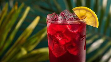 A bright red drink filled with ice cubes is garnished with a slice of lemon. It sits against a backdrop of lush green palm leaves, evoking a relaxing summer vibe perfect for warm days. photo