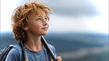 A young boy with red hair stands still, gazing into the distance with hiking poles resting at his side. photo