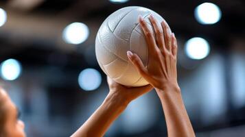 Two hands grip a white volleyball, ready for action in a vibrant gym. The focus captures the determination for a competitive play moment. photo