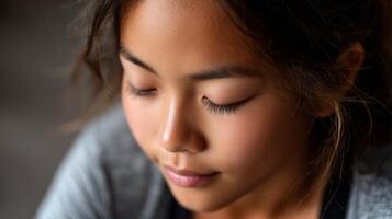 A young Asian girl practices yoga with a focused expression while performing a forward fold. Natural light highlights her calm demeanor and gentle features. photo