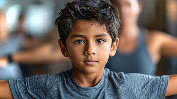 A South Asian boy executes the warrior II pose with concentration, practicing yoga among other students in a studio. The serene atmosphere enhances his focus. photo