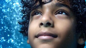 A South Asian boy is underwater, holding his breath with a peaceful expression. Bubbles surround him, creating a serene atmosphere in the pool. photo