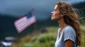 A girl with long hair stands at the edge of a lush green field, gazing thoughtfully as a flag flutters behind her on a cloudy day. photo