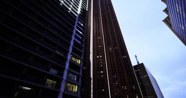 CGI Tall buildings towering over a city street at dusk with illuminated windows video