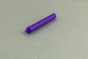 Purple crayon rests on a plain surface in bright lighting photo