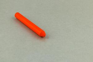 Bright orange crayon resting on a gray surface in daylight photo