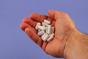 Hand holding white pills against a purple background photo