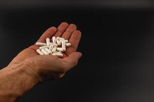 Hand holding white capsules against a dark background photo