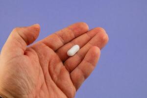 Hand holding a white pill against a blue background photo
