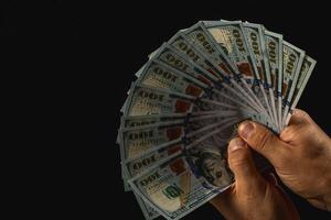 Hands displaying fanned hundred-dollar bills on black photo