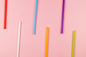 Colorful drinking straws arranged on a pink background photo