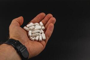 Hand holding white tablets on a dark background photo