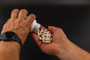 Person pouring white capsules from a bottle into hand photo