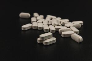 White tablets scattered on a dark surface in a close-up view photo