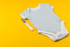 Baby onesie and pregnancy test on bright yellow background photo