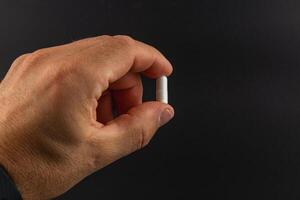 Person holds a small white capsule with one hand photo