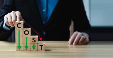 Business concept of cost reduction with stacked wooden blocks forming the word COST, descending arrow, representing expense control, financial optimization, strategic budgeting in corporate planning photo