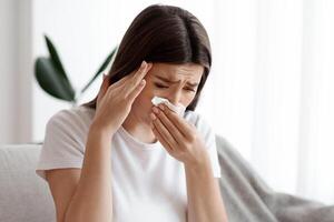 Pregnancy Illness. Sick Young Pregnant Woman Feeling Unwell At Home, Blowing Runny Nose In Tissue And Touching Temple, Suffering From Cold And Migraine, Upset Expectant Mother Sitting On Couch photo