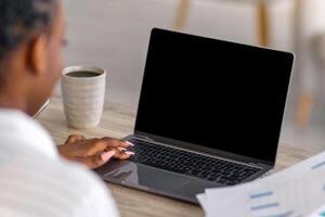 Back view of african american lady ceo or financial manager having online conference with her team from home, holding papers and looking at computer with blank screen, mockup, copy space photo
