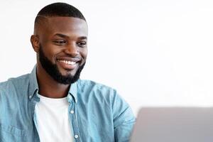 Black Millennial Male Entrepreneur Taking Notes While Working On Laptop In Office, African American Freelancer Guy Sitting At Desk Using Computer And Noting Down Information From Internet, Copy Space photo