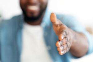 Unrecognizable Black Man Giving Hand For Handshake At Camera, Offering Partnership. Cropped Image Of Friendly African American Businessman Greeting Somebody, Extending Open Palm, Selective Focus photo