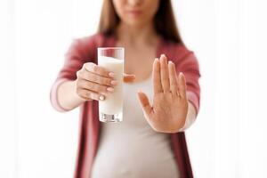 Unrecognizable Pregnant Woman Holding Glass Of Milk And Showing Stop Gesture With Open Palm At Camera, Expectant Lady Having Lactose Intollerance, Cropped Shot With Selective Focus, Copy Space photo