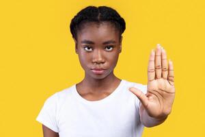 Determined African Woman Gesturing Stop Looking At Camera Warning And Forbidding Something Posing Standing Over Yellow Studio Background. Lady Protesting Against Bullying And Abuse. Selective Focus photo
