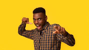 Gotcha. Excited Black Millennial Guy Pointing At Camera With Fingers, Funny Emotional African American Man In Checkered Shirt Indicating Somebody, Standing Isolated Over Yellow Background, Free Space photo