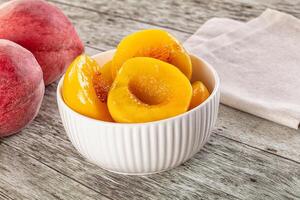 A bowl of peaches sitting on a table next to a peach photo
