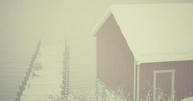 CGI Snowy winter mist envelops wooden cabin by frozen lake pier in serene landscape video