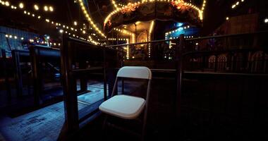 CGI Empty chair beside a carnival carousel illuminated by string lights at night video