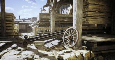 CGI Old wooden wheel rests beside weathered wooden structures in dusty settlement video