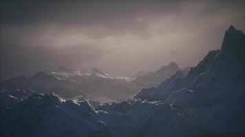 CGI Majestic snowy mountain range under a dramatic cloudy sky at dawn video