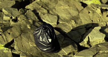 CGI Black trash bag resting on rugged rocks with greenish tint in natural light video