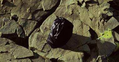 CGI Black trash bag resting on rocky surface in a natural setting video