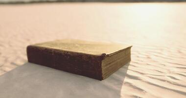 CGI Old book resting on soft sand under warm sunlight near a calm shoreline video