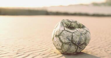 CGI Weathered soccer ball rests on sandy terrain during sunset video