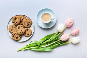 Cup coffee mug with coffee, cookies and tulips on a colored background. Greeting spring card top view photo