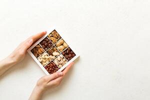 Young woman holding box with different nuts, closeup. Close up, copy space, top view, flat lay. Walnut, pistachios, almonds, hazelnuts and cashews photo