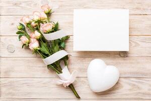 Greeting holiday card mockup with fresh roses on colored table background, mock up with copy space for design photo