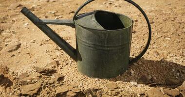 CGI Metal watering can resting on dry soil under bright sunlight in a garden video