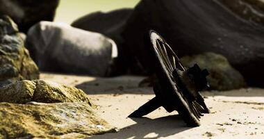 CGI Old wheel fragment rests among rocks on a sunlit sandy shore video