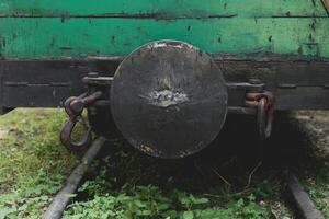 Close-up view of an antique train coupling on overgrown tracks surrounded by lush green vegetation in a forgotten railway yard photo