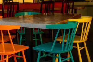 Colorful chairs surround a rustic table in a vibrant cafe setting during midday photo