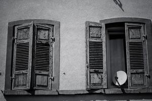 Weathered wooden shutters frame an open window in a quaint village, revealing a glimpse of rustic charm bathed in black and white hues photo