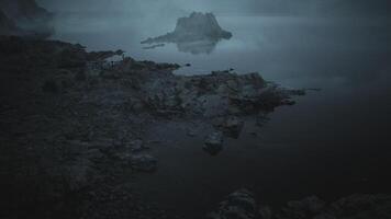 CGI Misty shoreline view with rocky island at dawn near calm water body video