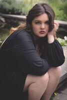 Subject is sitting by a serene pond in a natural setting during a bright day highlighting emotional expression and tranquility photo