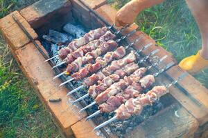 A man turns skewers of fresh pork meat on a brick barbecue in the yard of a house. Outdoor picnic with grilled shashlik. photo