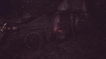 CGI Old wooden cart beside a rustic cabin in a dark forest setting at dusk video